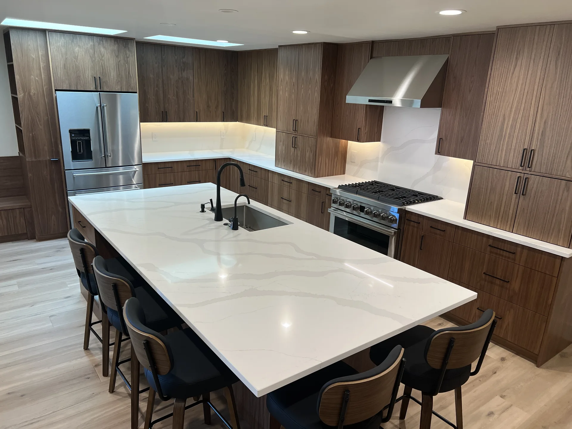 Kitchen with a long white quartz waterfall island, walnut cabinetry, full-height veined slab backsplash, stainless range and hood